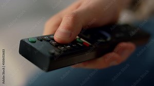 Fingers pushing remote control buttons closeup. Unknown man switching channels.