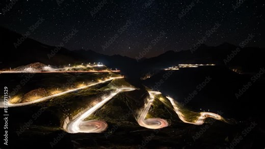 Long exposure night shot shows a winding road lit by lights with car trails against a starry sky