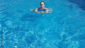 a young beautiful woman with red hair and a blue swimsuit swimming in a luxury outdoor pool on a Sunny summer day. super slow motion.