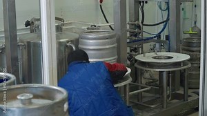 Labourer places a small barrel into the industrial washing equipment. Washing the beer barrels with factory equipment. Turning on the automated equipment to wash metal barrels at the plant.