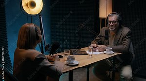 Medium full shot of middle-aged Caucasian male business podcast host conducting interview for show streaming online with female company CEO or entrepreneur, discussing secrets of success