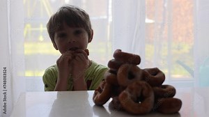 Cute school child, boy, eating doughnuts at home, homemade fresh donuts with sugar.