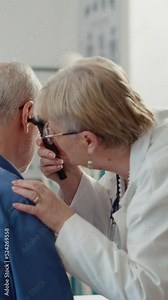 Vertical video: Otolaryngology specialist using otoscope to examine ear infection, helping patient with disease. Otology instrument to do ent consultation for audiology diagnosis in medical office.