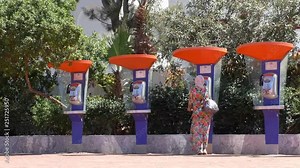 Rear view of a woman wearing long flower pattern dress and scarf is using public pay phone or payphone at a tropical holiday resort
