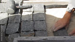 Work on laying natural granite paving stones. A male worker installs granite cobblestones for a sidewalk, yard landscaping, patio or other street design, video without sound