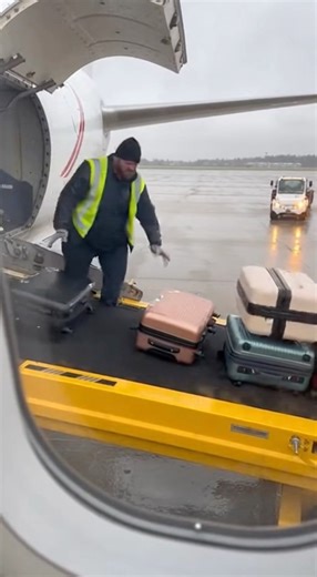Airport baggage handler loses footing while unloading luggage in tarmac mishap CHARLOTTE, NORTH CAROLINA — A ramp-area camera captured a brief workplace incident involving an airport baggage handler during routine unloading operations from a commercial aircraft. The footage shows luggage moving steadily along a conveyor belt positioned at the cargo hold of a parked plane. As bags continue to come down the belt, the worker appears to reposition quickly while handling multiple pieces at once. In t