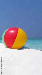 Colorful inflatable beach ball on the sandy beach on blue sky ad water background