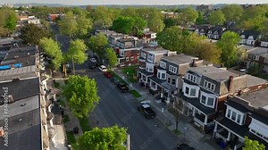 Aerial footage of a quiet residential neighborhood with tree-lined streets, charming row houses, and parked cars. American city suburb row houses.