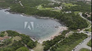 Drone orbits to the left over beach as camera pans down to focus on beach, then pans back up to reveal town and rest of surrounding area