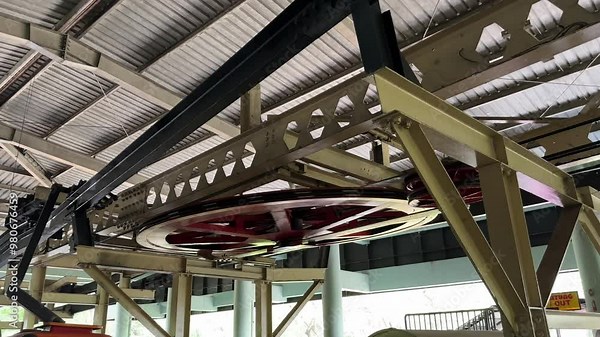 close up view of The large wheel mechanism of the cable car system is getting ready to go. The cable car starts moving slowly on the hanging rail, ready to cross its track.