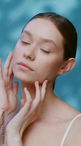 A young woman without makeup touches the clean skin of her face