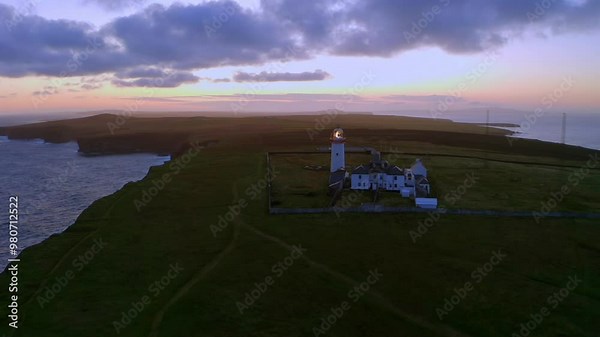 Aerial pullback reveals a stunning twilight sky with Loop Head lighthouse beaming in the foreground