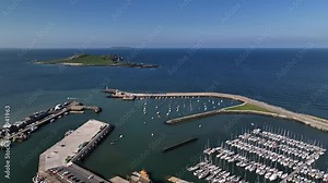 Howth Harbour, County Dublin, Ireland, May 2023. Drone pushes forward above the harbour Marina over the Pier and Lighthouse with Ireland's Eye in background with Lambay Island in the distance.