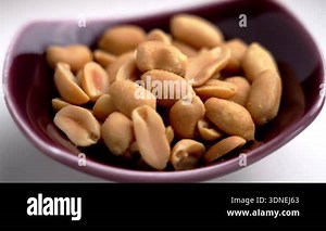 A serving of salted roasted peanuts in a ceramic bowl on a white kitchen table. Rotation