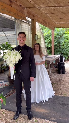 Groom stands eagerly with a bouquet in hand, trying to guess the details of his bride’s dress
