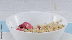 Close up of a healthy cereal, grain and dry strawberry dropping or falling in to bowl. Side view of white bowl with yellow cornflake, dry fruit. Macrography. Slow motion. Breakfast concept. Pabulum.