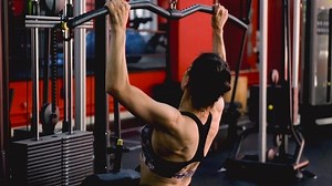 A middle-aged woman trains her arm muscles using a simulator in the gym.