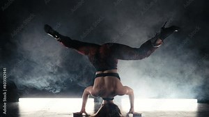 Strong woman dancing legs while standing on head. Amazing hot dance in dark studio. Lady dancer in tight clothes and heels. Headstand