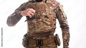 Man in combat camouflage and body armor inserts rifle magazines into the pouches on the plate carrier