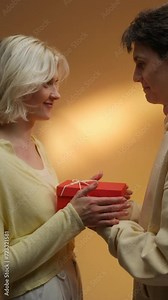 Happy man giving gift to his girlfriend on beige studio background, free space.