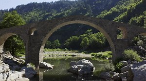 Approaching drone shot passing through the main arch of the Devil's Bridge over the Arda River located in the town of Ardino near the Rhodope Mountains in Bulgaria.