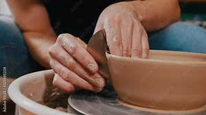 Man potter sculpting a pot out of clay auxiliary using scapula - removes excess from the sides