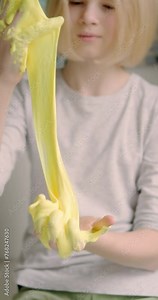 Child delightfully playing with homemade yellow slime, stretches slime to the sides, an engaging sensory activity, concept for educational content, toy stores, and child development at home