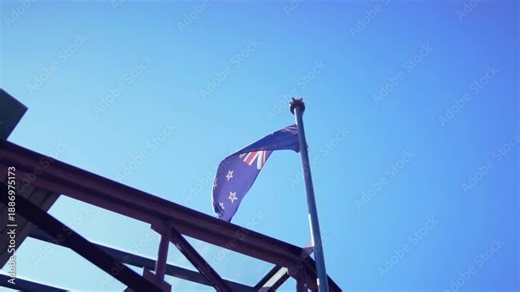 The New Zealand flag dances elegantly in the breeze. This sharp capture highlights the deep blue field and iconic red stars, embodying Kiwi pride and Pacific spirit under a pristine sunny sky.