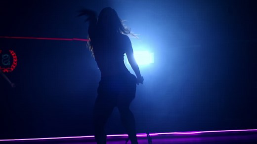 Female silhouette moving gracefully in front of projector. Long-haired dancer in dark room. | Premium Stock Video Footage