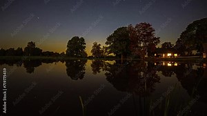 Sunset over a mirror lake with a country house on the shore. Time lapse shot.