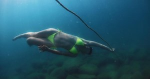 Beauty woman swims without diving fins underwater in transparent blue lake