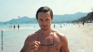 Tanned man takes off sunglasses looking with confident look that gives special magnetism. Confident look exudes charisma and attractiveness. Millennial looks straight into, showing off confident pose.