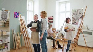 Group of senior people with teacher painting pictures in art class.