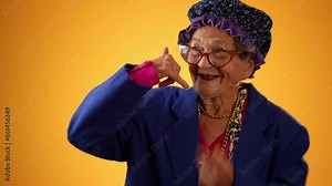 Funny view of smiling happy elderly senior old woman with wrinkled skin smiling pointing and giving call me gesture with hands isolated on solid yellow background.
