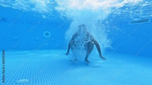 Man jumps under water in the pool. Underwater view on a man diving into water and swimming inside the swimming pool.