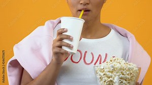Excited girl drinking beverage from paper cup and holding popcorn bowl, cinema
