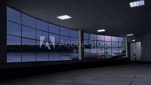 A winter vacation clip of an empty airport terminal in the night with a propeller airplane in snowfall behind window ready for boarding and a big aircraft landing in the background