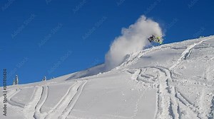 the pilot makes large jumps on a snowmobile in a mountain valley on a background of blue sky and white snow. cool snowmobiler flies and lands with snow storm spray and whirlwinds. snowmobilers sports