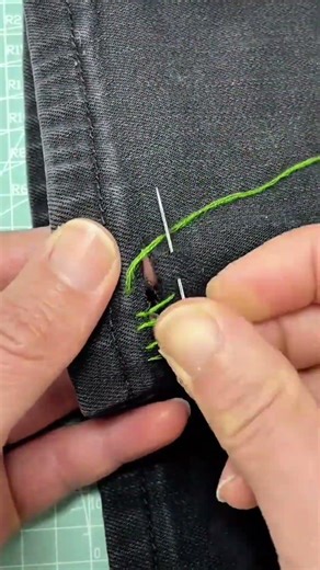 sewing and repairing a hole in black denim pants using green thread and a sharp metallic needle