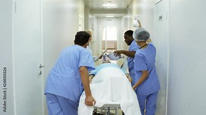 Following dolly shot of emergency room nurses administering oxygen and IV fluids to unresponsive patient on gurney and rushing him into surgery as female doctor giving instructions