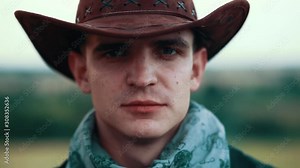 Shot of young cowboy smoking cigar look at camera serious on field hat adventure american culture authority portrait face close up slow motion Stock Video