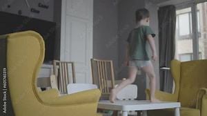 little boy kid jumping chairs armchairs table indoors living-room create new game himself. developing skills physical health at home. games without toys, playing furniture climb jump obstacles concept