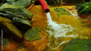 Mineral water comes out of the plastic pipe .Cascades in rapid stream of mineral water. Red ferric sediments on big boulders between green ferns. Red plastic tube Stock Video