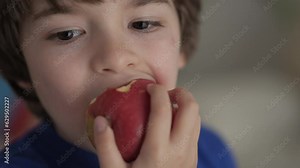 Cute Little Boy Eating Red Apple. Child Eats Fruit. Kid Bites Fruit and Chews Looking at Camera in Kitchen. Healthy Diet Vegetarian. Healthy Nutrition Child Development. Happy Boy Biting Eating Apple.