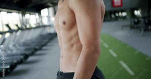 Cropped view on athletic shirtless male body with abs and obliques at gym. Closeup of handsome man torso with muscles at fitness club