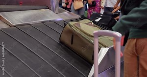 Various suitcases emerge and slide down on baggage carousel in airport arrival hall. Automated system pauses new bags if conveyor is full, then lowers them into available space