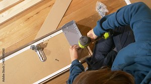 TOP DOWN: Unrecognizable woman uses a power drill while screwing together metal hinges on a closet door. Young Caucasian female assembles her furniture herself while moving into her brand new house.