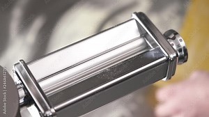 A close-up of dough flatten machine and a hand setting the thickness, and then putting a piece of dough for processing. Fresh noodles preparation in a restaurant