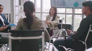 Confident business woman in wheelchair presenting during business meeting with colleagues.