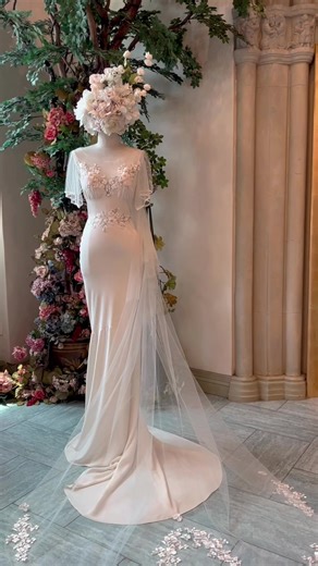 The Merlot Gown styled with the Odessa Veil 👰‍♀️🍃 A classic and romantic look, this crepe sheath wedding dress is made in a soft mermaid silhouette with an illusion neckline and a sheer low back finished with tulle sputter sleeves 🤍 Detailed with delicate embroidered ivory and silver florals for a whimsical touch #clairepettibone #weddingtok #weddingdressshopping #floralweddingdress #classicwedding